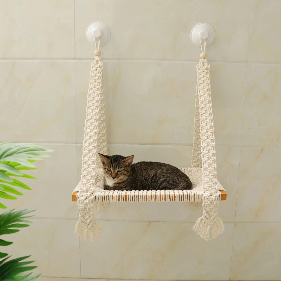 Macrame cat hammock in a cream beige cotton with a small black and grey striped cat sitting in it.
