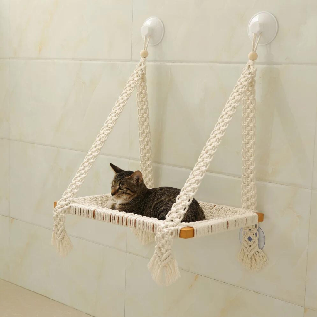 Macrame cat hammock in a cream beige cotton with a small black and grey striped cat sitting in it.