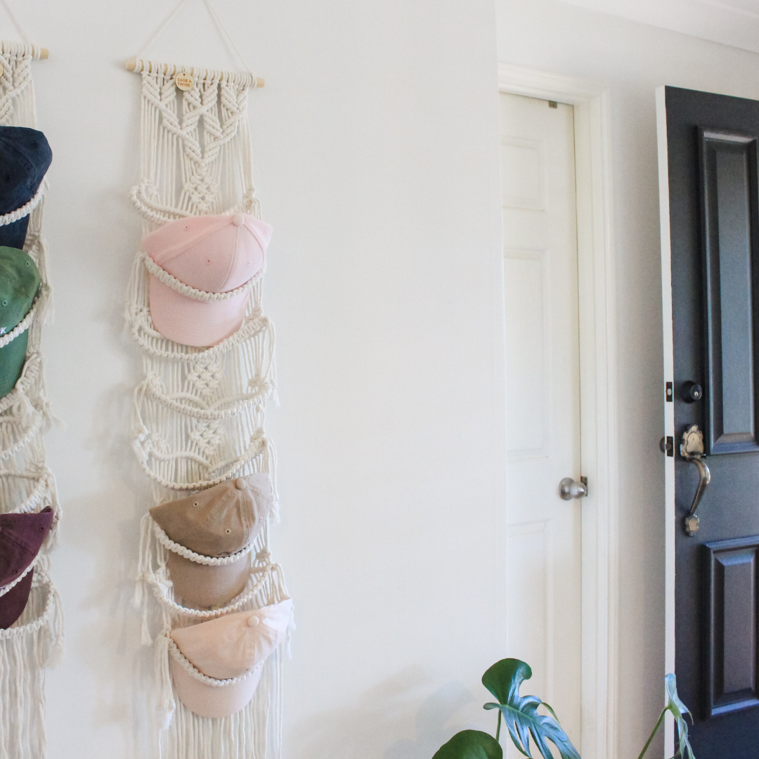 macrame cap hangers, hanging in the front entrance of a home. both macrame cap hangers hold half a dozen baseball caps