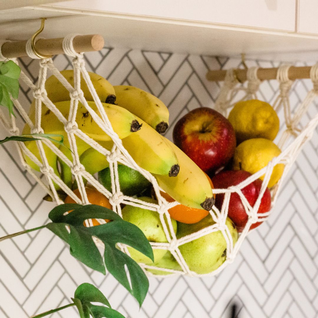 close up of the cotton macrame woven intricately and beautifully in a macrame fruit hammock made for a van life or caravan or kitchen. A macrame fruit hammock holding bananas apples lemons oranges and pears hanging from a kitchen cabinet. handmade by Sage and twine . Australian Owned