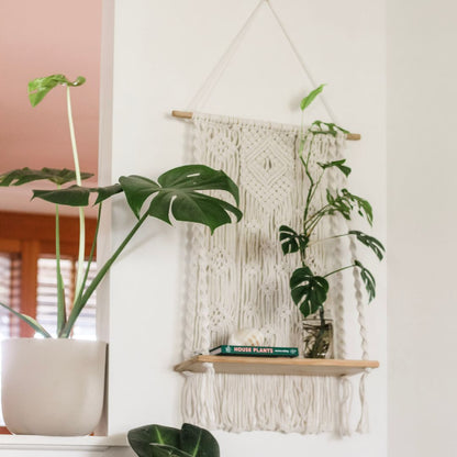 a room with white walls and pot plants and a white macrame shelf with decor items decorated. the shelf has intricate cotton craftsmanship