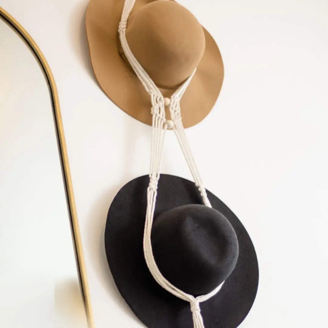 black hat and brown hat against white background being held be a macrame hat rack.